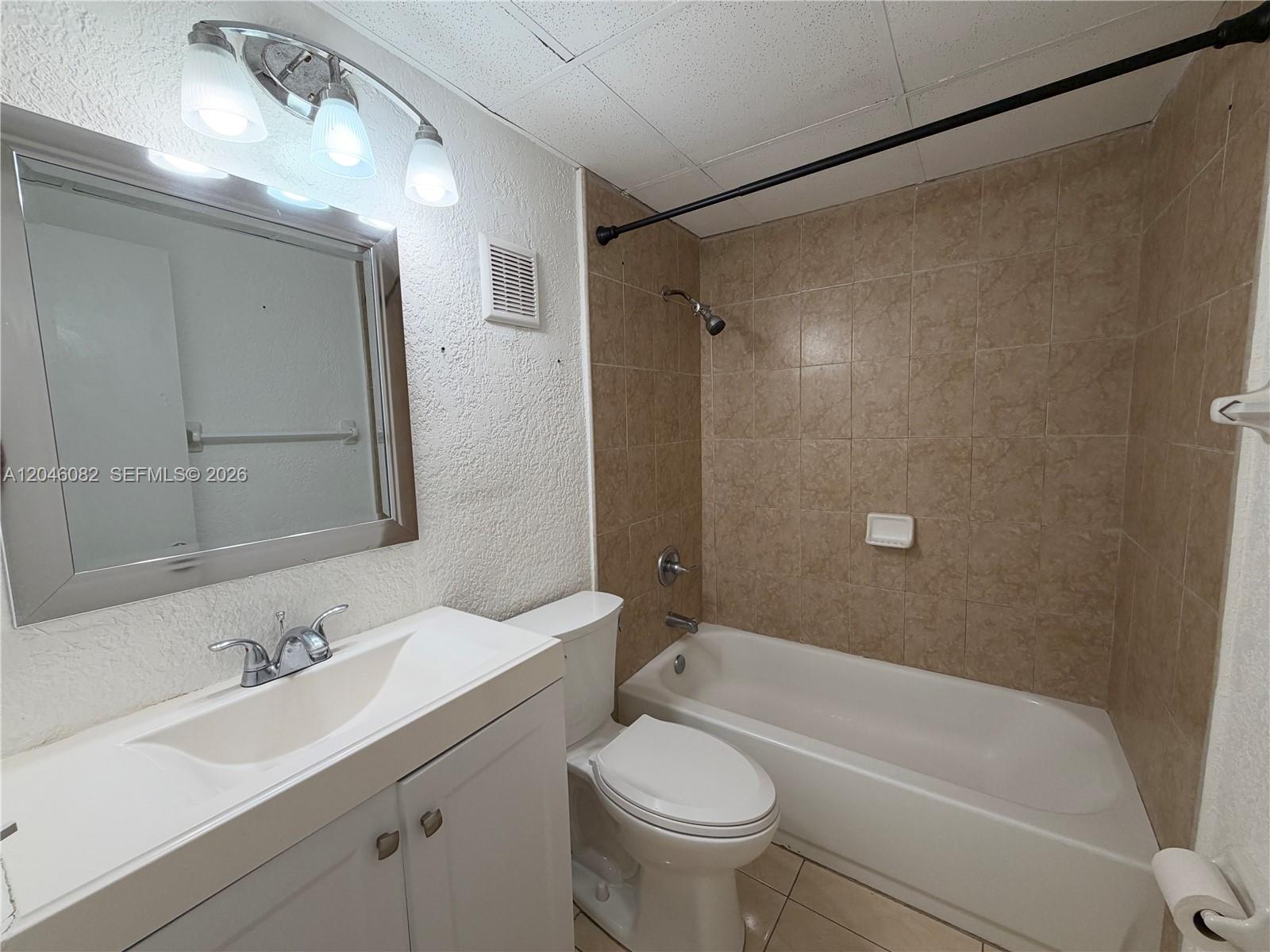 A bathroom features a white vanity, a toilet, and a bathtub with tan tiled walls — 5960 NE 5th Ct # 2, Miami FL 33137, MIAMI, FL