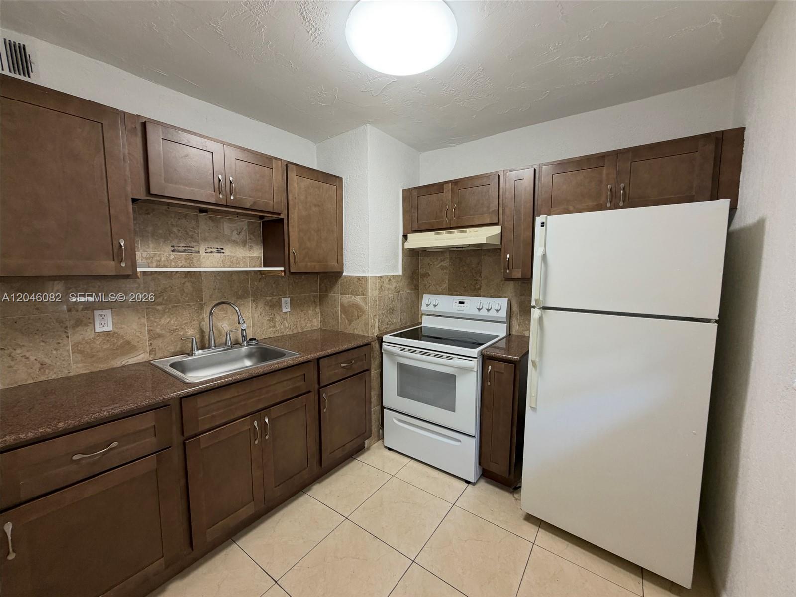 This kitchen features brown cabinets, granite countertops, a white stove, and a white refrigerator — 5960 NE 5th Ct # 2, Miami FL 33137, MIAMI, FL