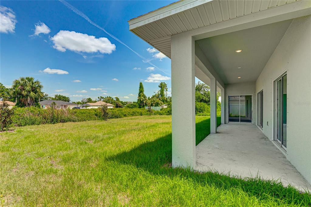 A covered concrete patio overlooks a grassy backyard under a bright blue sky — 2194 BRANCUSI AVENUE, NORTH PORT, FL