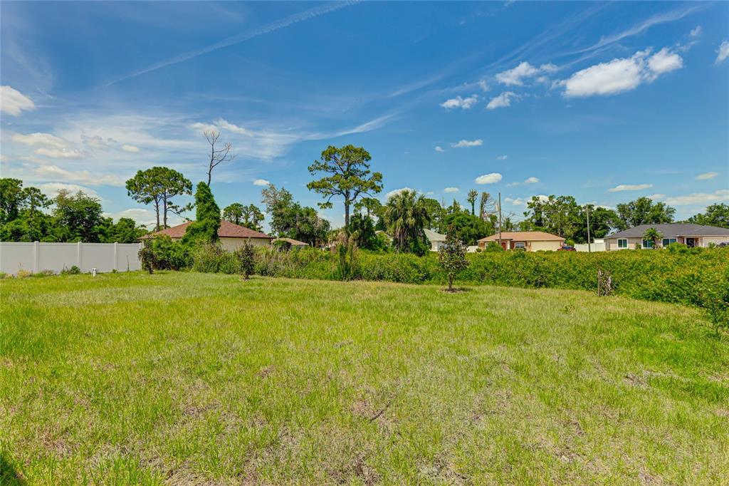 A grassy, vacant residential lot features scattered small trees and a white privacy fence — 2194 BRANCUSI AVENUE, NORTH PORT, FL
