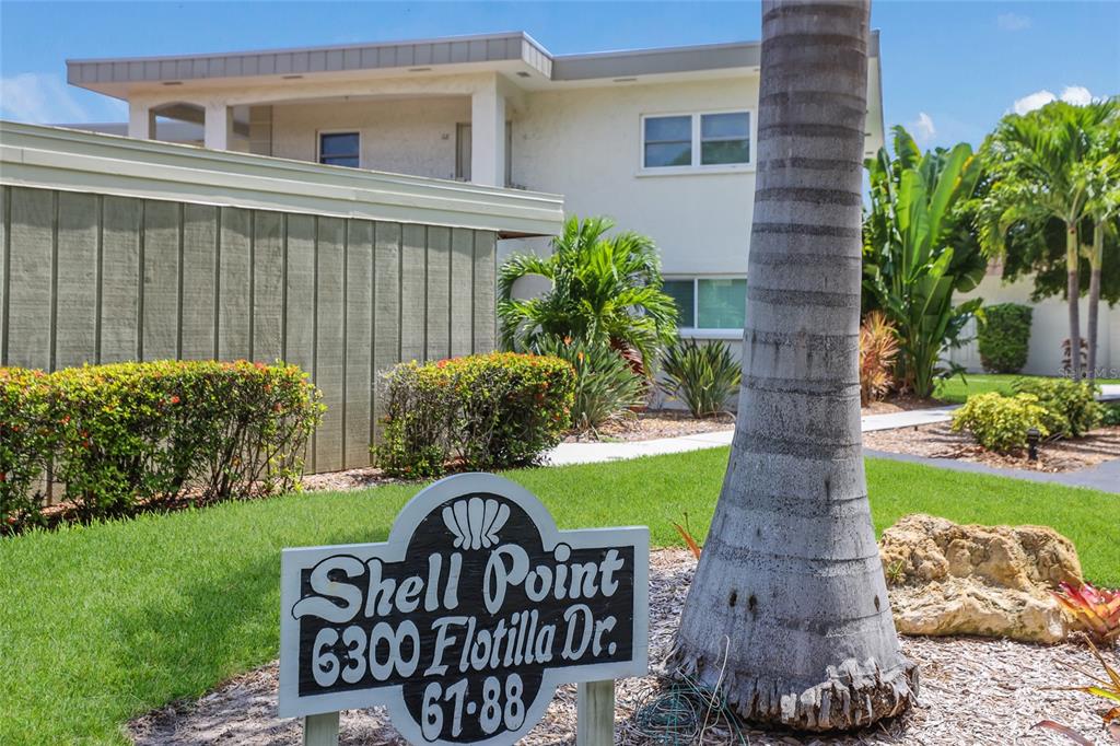 A sign for a residential complex stands in front of a two-story building with landscaping — 6300 FLOTILLA DRIVE UNIT 107, BRADENTON BEACH, FL