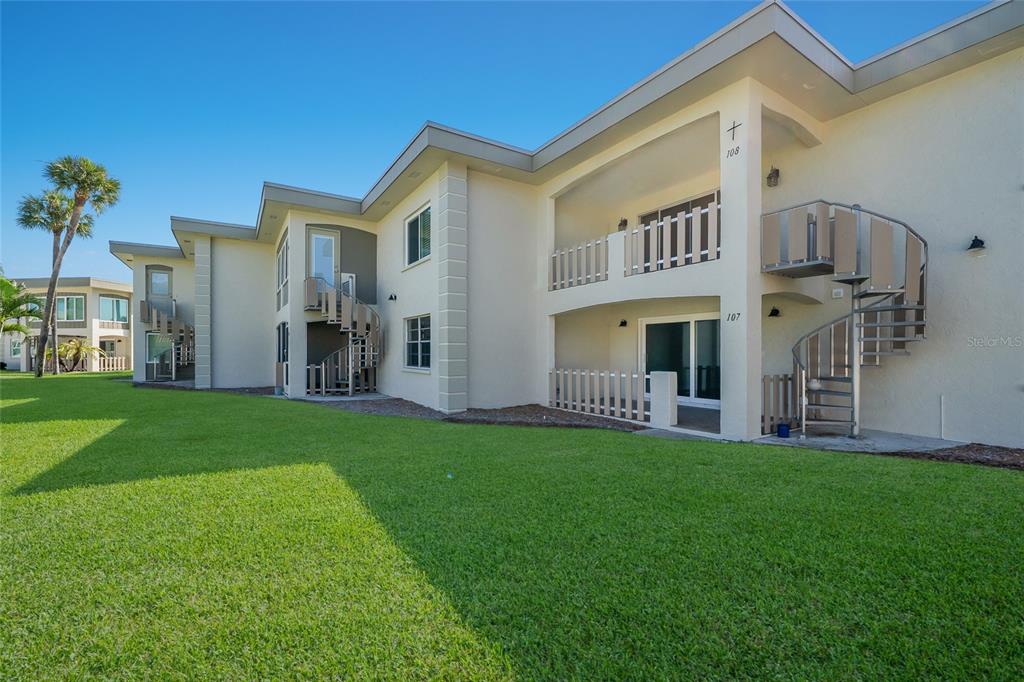 A two-story apartment building features exterior spiral staircases and balconies on a grassy lawn — 6300 FLOTILLA DRIVE UNIT 107, BRADENTON BEACH, FL