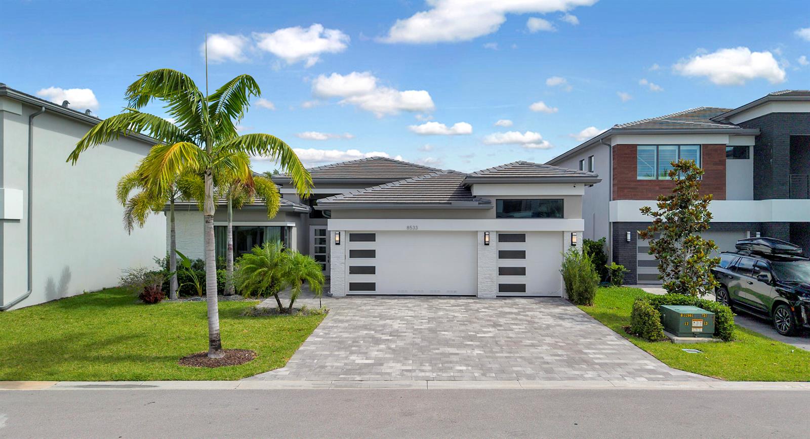A modern one-story house with a paved driveway, a three-car garage, and a palm tree — 8533 Ganton Drive, Boca Raton FL 33434, BOCA RATON, FL