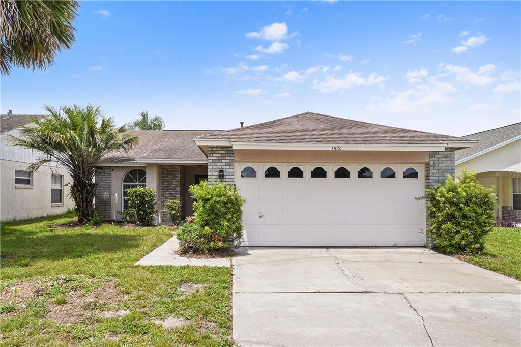 A single-story house with a white garage door, tan stucco walls, and a palm tree — 1512 OAK HILL TRAIL, KISSIMMEE, FL