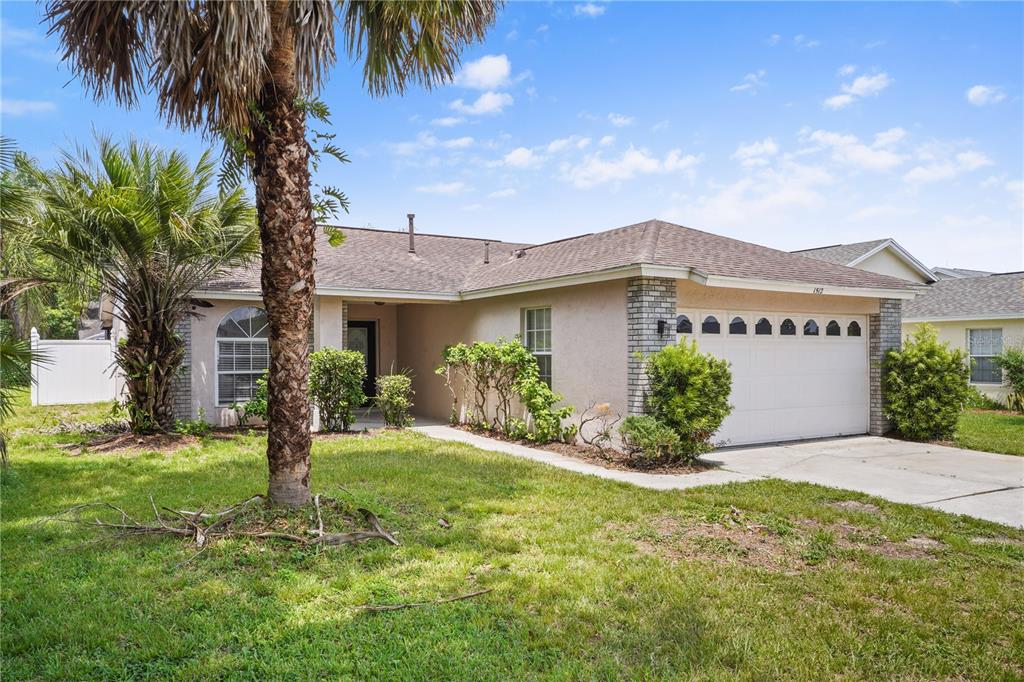 A single-story house with a beige stucco exterior, a two-car garage, and a palm tree — 1512 OAK HILL TRAIL, KISSIMMEE, FL