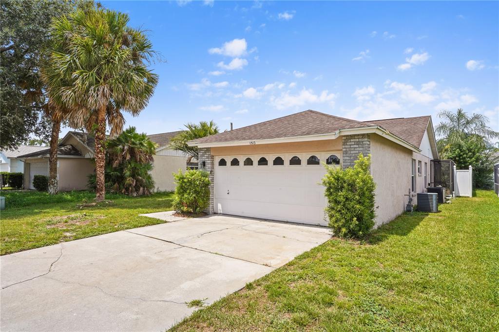 A single-story house with a white garage door, tan stucco walls, and a concrete driveway — 1512 OAK HILL TRAIL, KISSIMMEE, FL