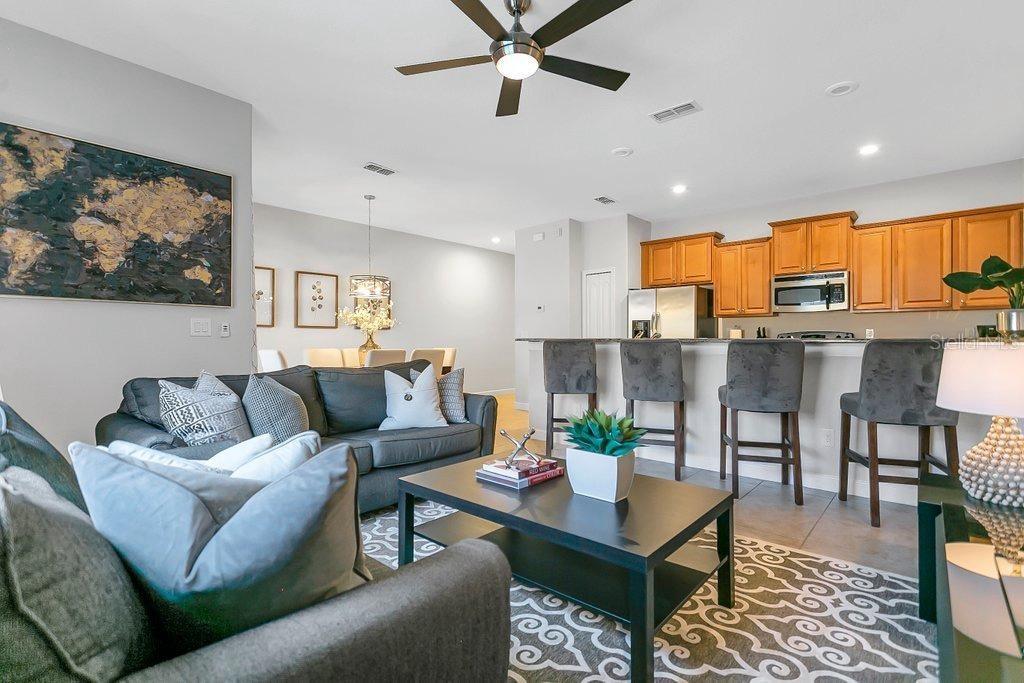 An open-concept living room and kitchen featuring grey sofas, a breakfast bar, and wooden cabinets — 8979 CALIFORNIA PALM ROAD, KISSIMMEE, FL