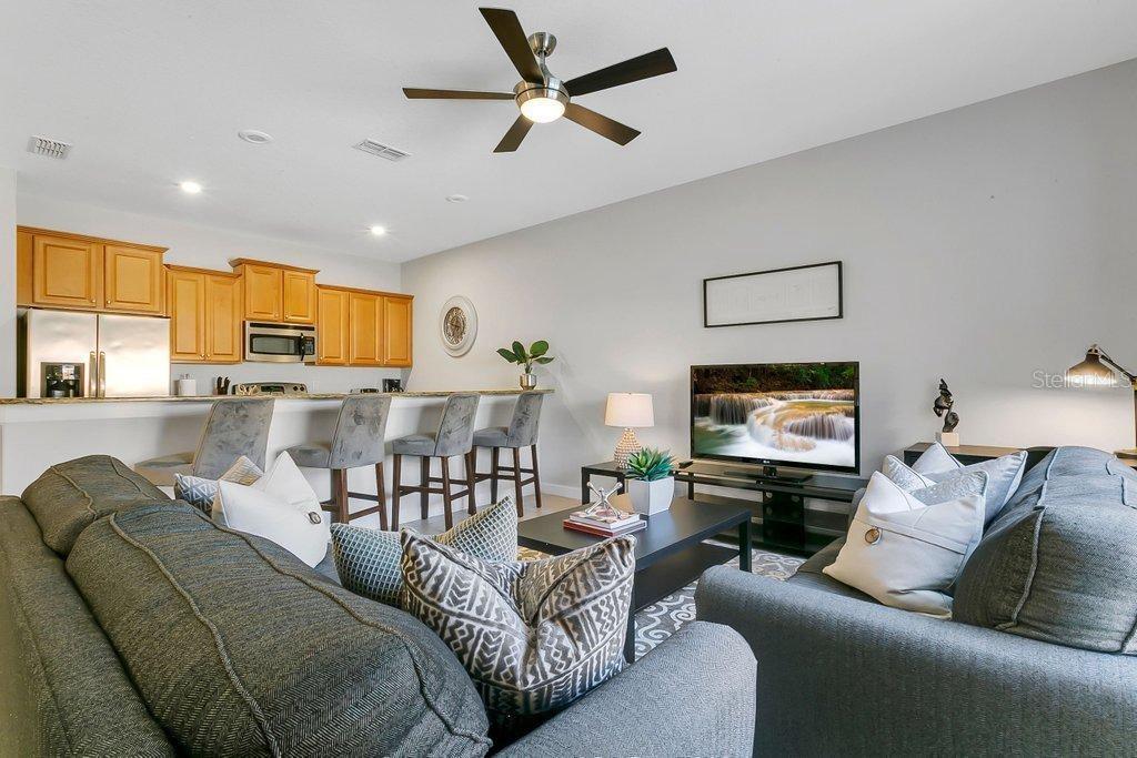 A living room with a gray sofa faces a television and an open-concept kitchen — 8979 CALIFORNIA PALM ROAD, KISSIMMEE, FL