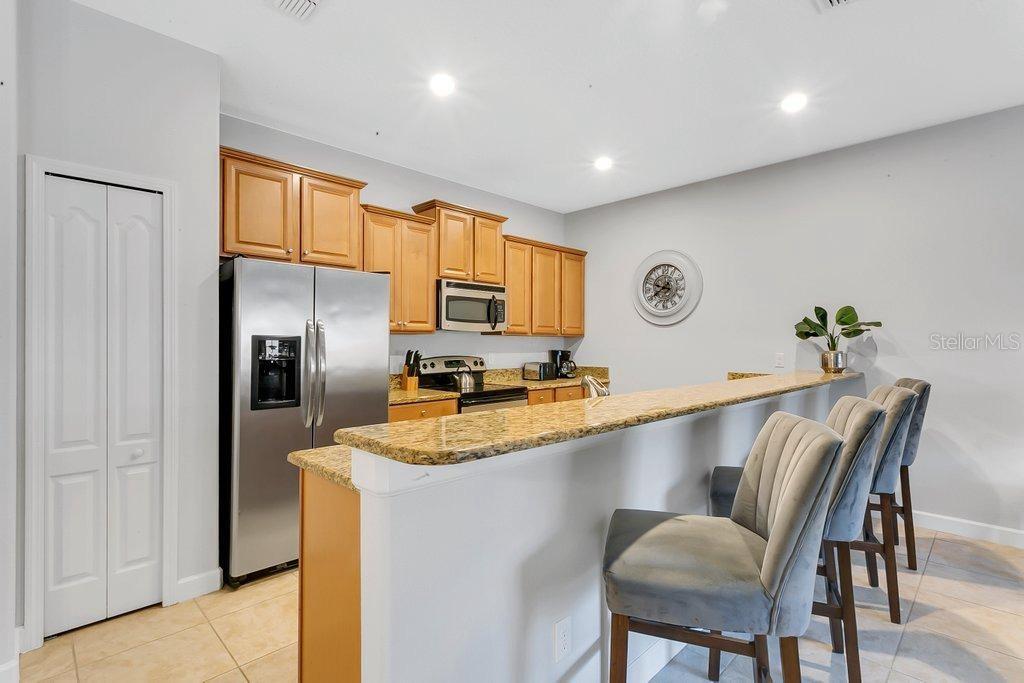 A kitchen features light wood cabinets, granite countertops, stainless steel appliances, and a breakfast bar — 8979 CALIFORNIA PALM ROAD, KISSIMMEE, FL