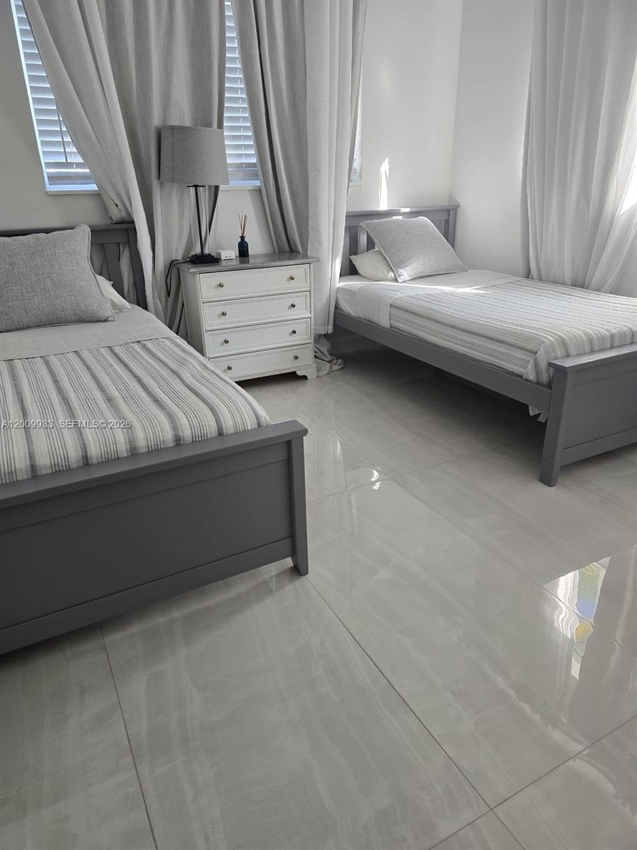 A bedroom features two gray twin beds, a white nightstand, and light-colored tile flooring — 1030 NE 83rd St # 0, Miami FL 33138, MIAMI, FL
