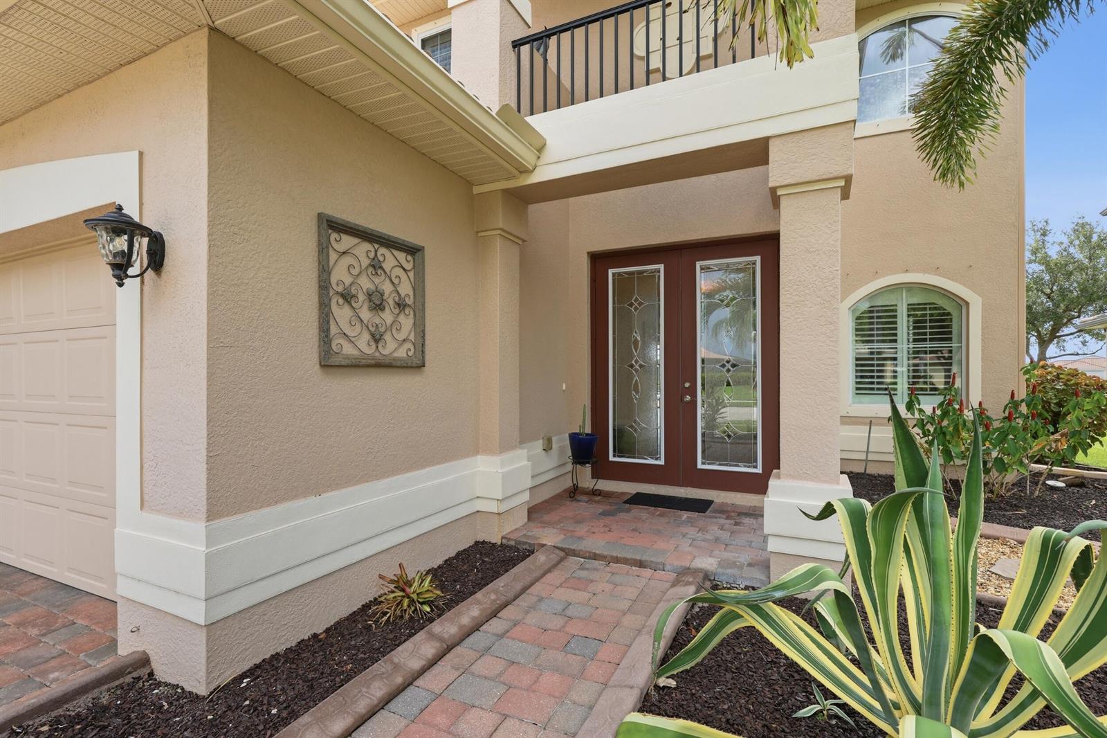 A beige two-story house exterior features a brick walkway leading to a double front door — 1517 Birdie Drive, Naples FL 34120, NAPLES, FL