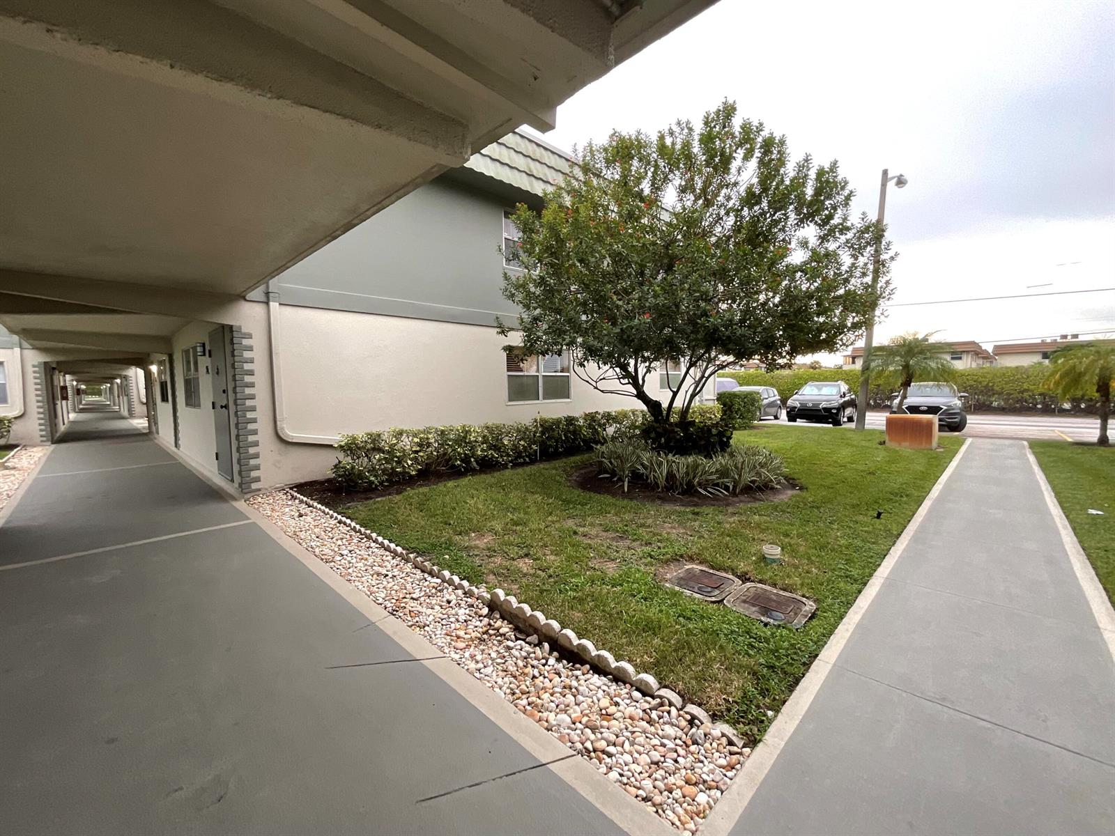 An exterior view shows a covered walkway, a grassy lawn with a tree, and parking — 679 Saxony Way, Delray Beach FL 33446, DELRAY BEACH, FL