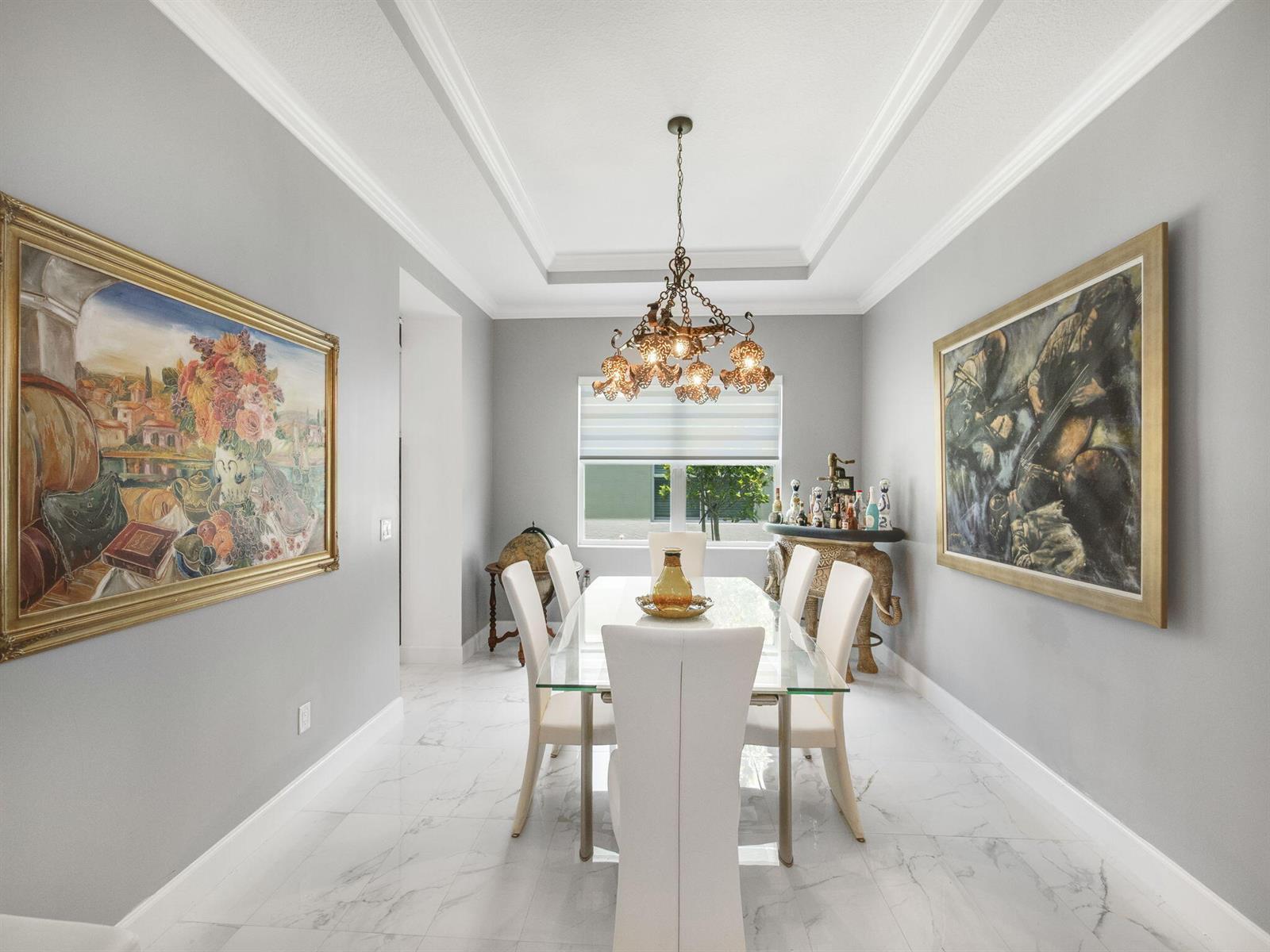 A dining room features a glass table, white chairs, a chandelier, and two large paintings — 5857 Whippoorwill Circle, Westlake FL 33470, WESTLAKE, FL