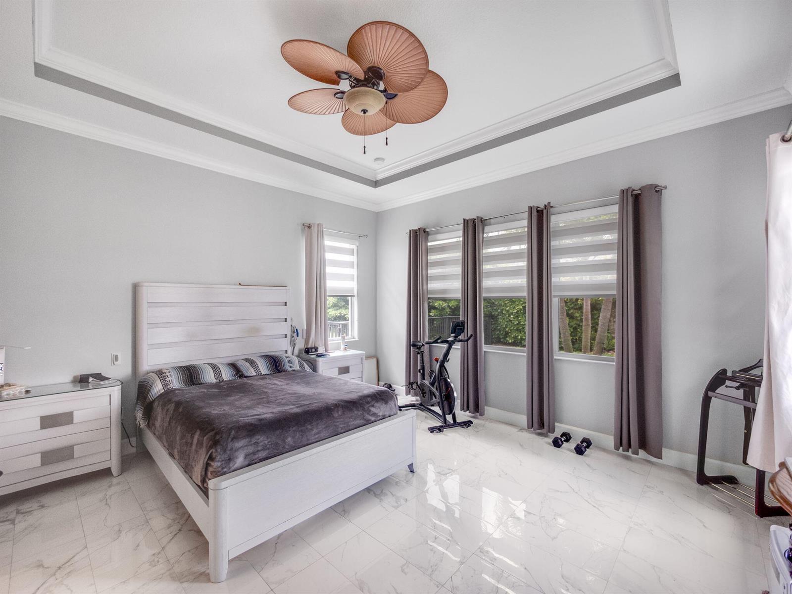 A bedroom features a white bed, marble floors, a ceiling fan, and a stationary bike — 5857 Whippoorwill Circle, Westlake FL 33470, WESTLAKE, FL