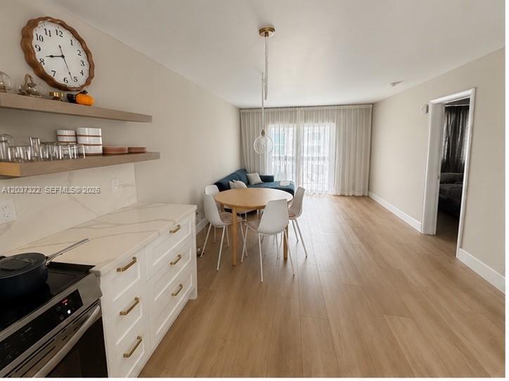 A kitchen with white cabinets and floating shelves opens into a dining and living area — 220 Washington Ave # 5C, Miami Beach FL 33139, MIAMI BEACH, FL