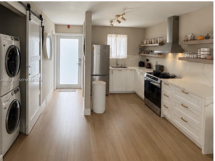 A kitchen features white cabinets, stainless steel appliances, open shelving, and a stacked laundry unit — 220 Washington Ave # 5C, Miami Beach FL 33139, MIAMI BEACH, FL