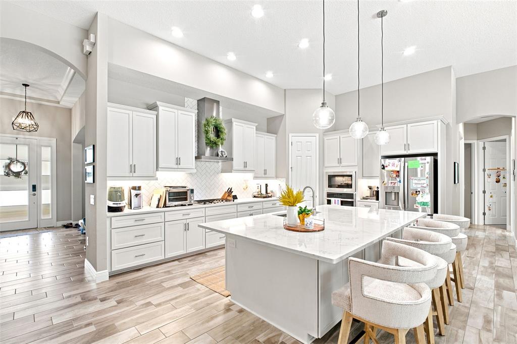 A bright, modern kitchen features white cabinetry, a large marble-topped island, and light wood flooring — 4263 WOODLAND RETREAT BOULEVARD, NEW PORT RICHEY, FL