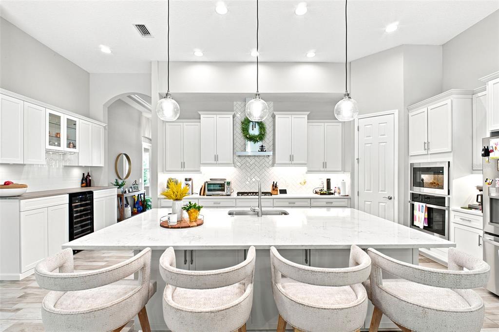 A bright, modern kitchen features a large white marble island, pendant lighting, and white cabinetry — 4263 WOODLAND RETREAT BOULEVARD, NEW PORT RICHEY, FL