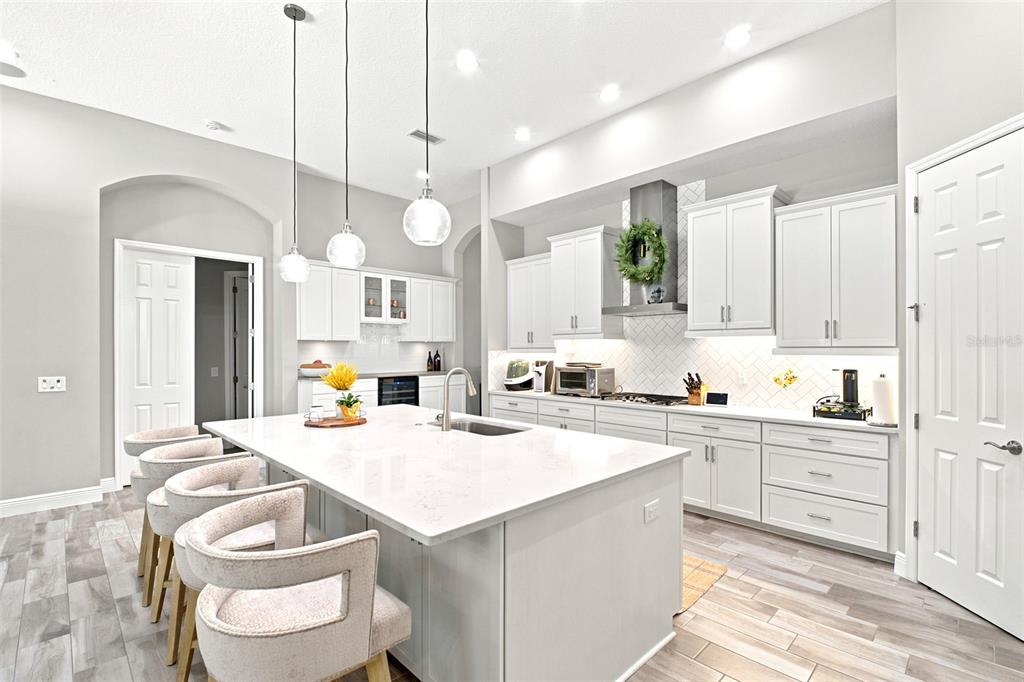 A bright, modern kitchen features white cabinetry, a large quartz island, and pendant lighting — 4263 WOODLAND RETREAT BOULEVARD, NEW PORT RICHEY, FL
