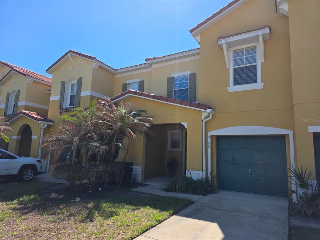A two-story yellow stucco townhouse features a green garage door and a covered entryway — 5160 AMBERGRIS LOOP, KISSIMMEE, FL