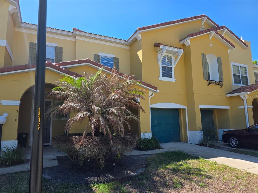 A yellow two-story townhouse features a palm tree in the front yard and a garage — 5160 AMBERGRIS LOOP, KISSIMMEE, FL