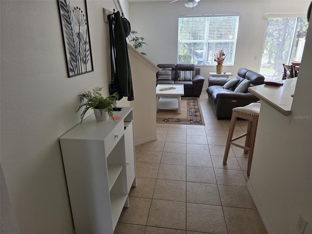 A tiled entryway leads into a living room with brown leather sofas and a window — 5160 AMBERGRIS LOOP, KISSIMMEE, FL