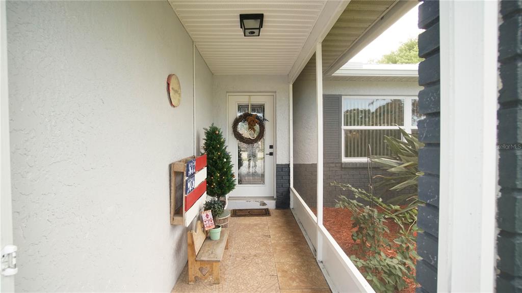 A covered outdoor entryway features a screened-in porch, a wooden bench, and a front door — 2550 FULTON COURT, MELBOURNE, FL
