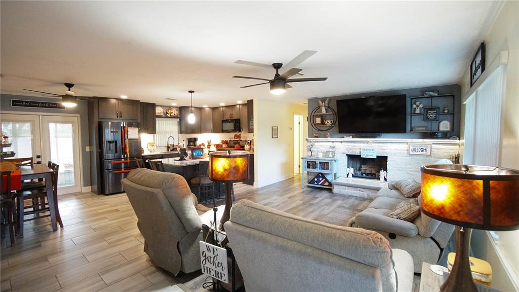 An open-concept living room and kitchen featuring gray wood-look flooring and a stone fireplace — 2550 FULTON COURT, MELBOURNE, FL