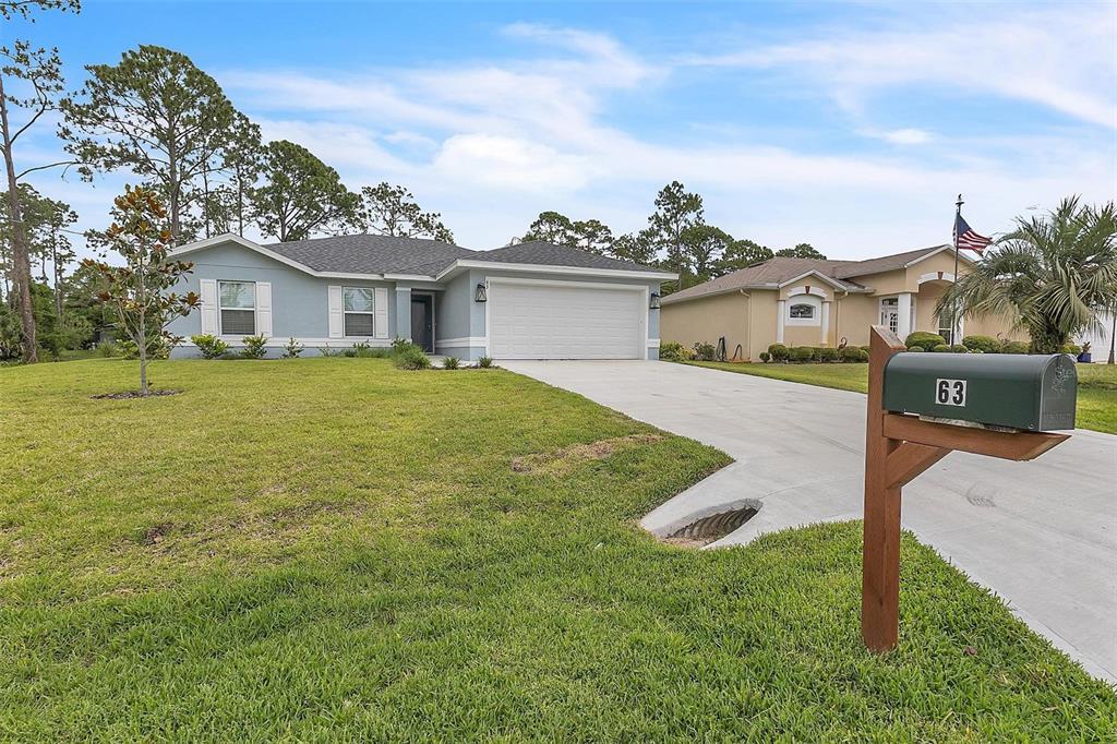 A light blue single-story house with a two-car garage and a wooden mailbox in front — 63 PRESIDENT LANE, PALM COAST, FL