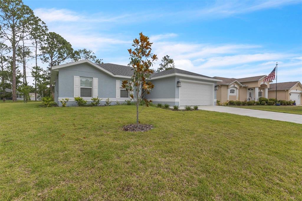 A light blue single-story house with a two-car garage and a front yard tree — 63 PRESIDENT LANE, PALM COAST, FL