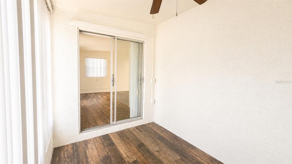 A sunroom features wood-look flooring, white textured walls, and a sliding glass door — 6165 58TH STREET N UNIT 3G, ST PETERSBURG, FL