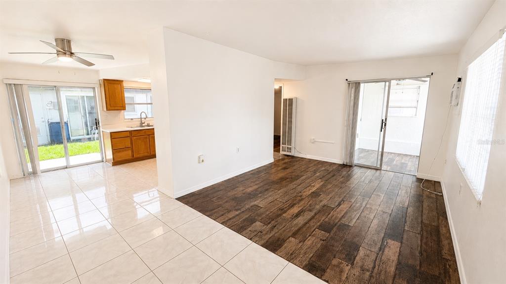 A living room with wood-look flooring transitions into a tiled kitchen area with sliding doors — 6165 58TH STREET N UNIT 3G, ST PETERSBURG, FL