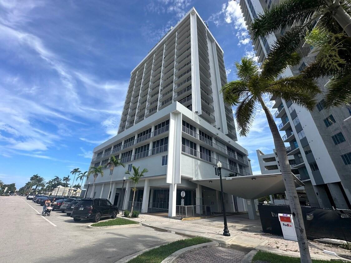 A tall, modern white apartment building stands next to a parking lot and palm trees — 1720 E Harrison Street # A, Hollywood FL 33020, HOLLYWOOD, FL