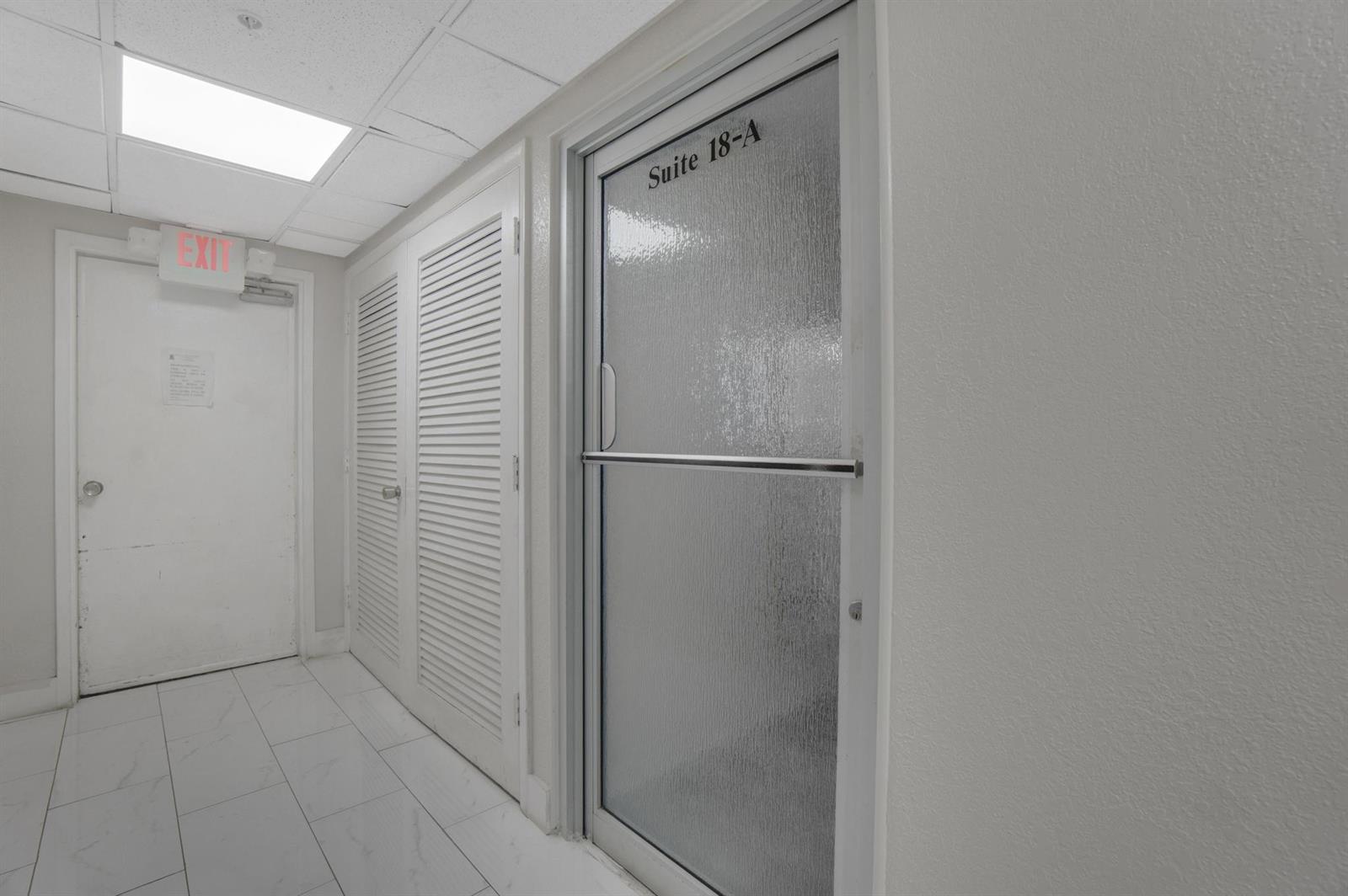 A hallway features white tiled floors, an exit door, louvered closet doors, and a glass-paneled suite door — 1720 E Harrison Street # A, Hollywood FL 33020, HOLLYWOOD, FL