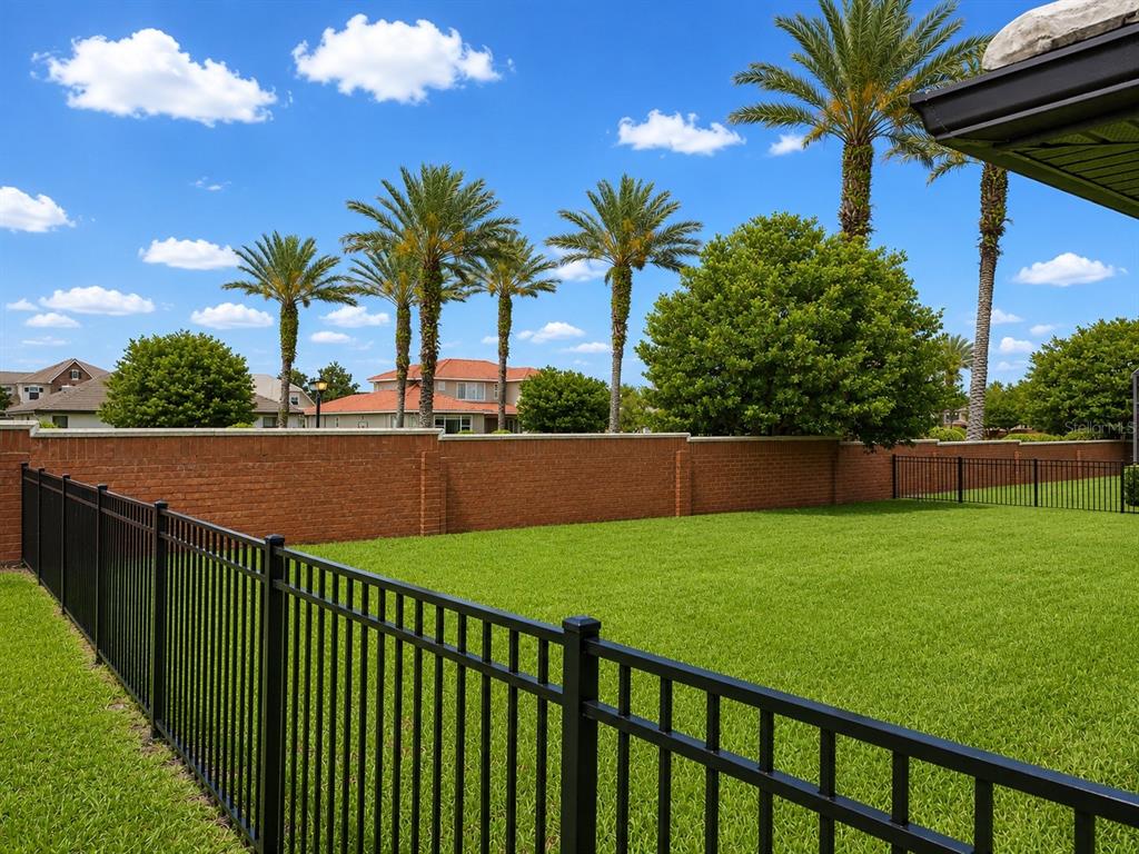 A fenced backyard features a green lawn, a brick wall, and several tall palm trees — 226 LAKE VISTA DRIVE, AUBURNDALE, FL