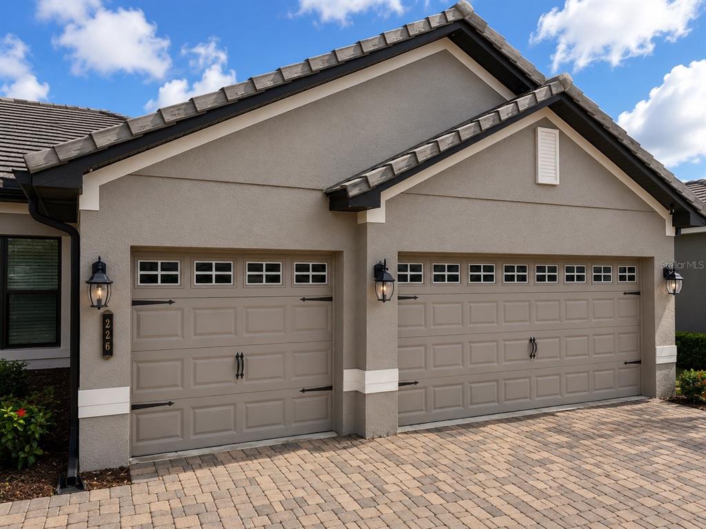 A two-car garage with beige doors, decorative hardware, and lanterns on a paved driveway — 226 LAKE VISTA DRIVE, AUBURNDALE, FL