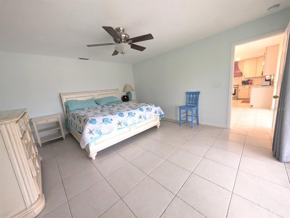 A bedroom with light-colored tile flooring, a white bed frame, and a ceiling fan — 50 CADDY ROAD, ROTONDA WEST, FL
