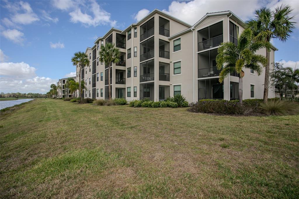 A multi-story apartment building with screened balconies sits next to a grassy lawn and water — 18028 GAWTHROP DRIVE UNIT 403, BRADENTON, FL