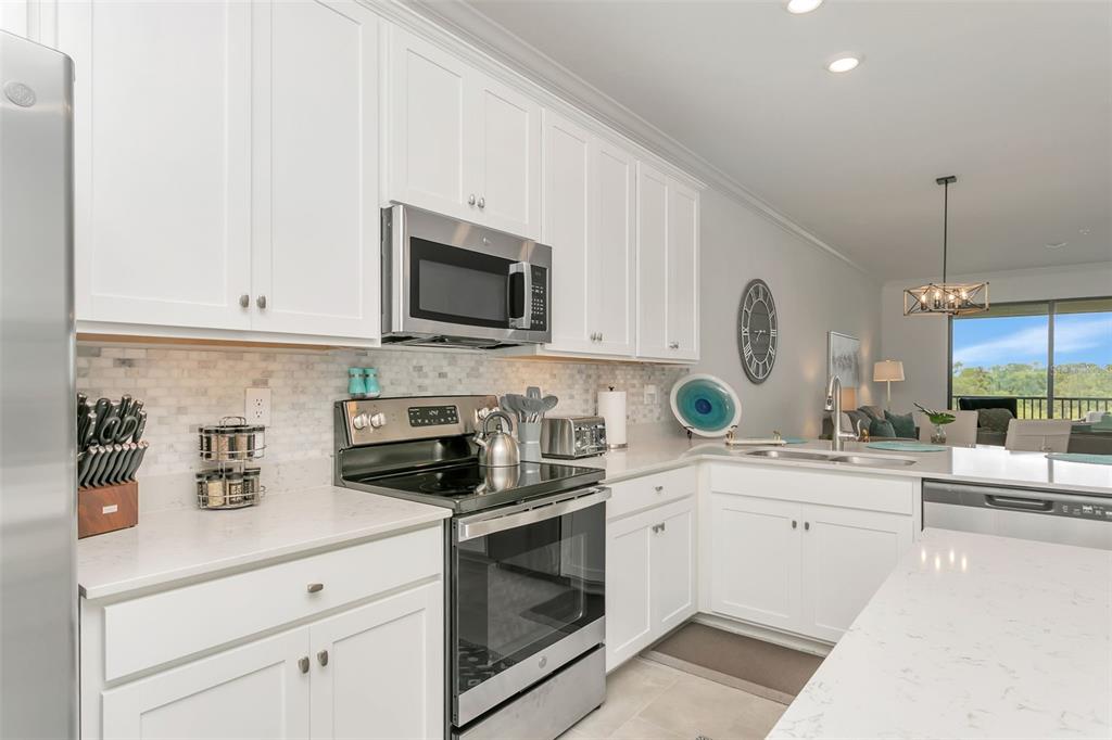 A modern kitchen features white cabinets, stainless steel appliances, and light-colored quartz countertops — 18028 GAWTHROP DRIVE UNIT 403, BRADENTON, FL