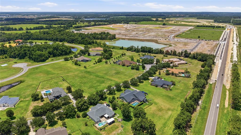 An aerial view shows several houses with pools surrounded by green lawns and a construction site — 9853 PREAKNESS STAKES WAY, DADE CITY, FL