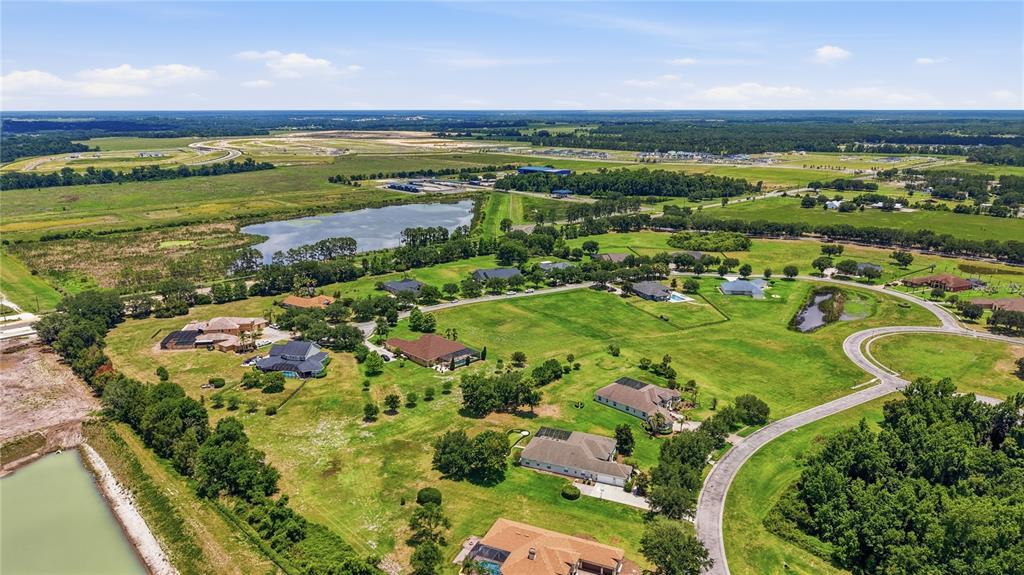 An aerial view shows several houses situated on large, grassy lots near a lake — 9853 PREAKNESS STAKES WAY, DADE CITY, FL