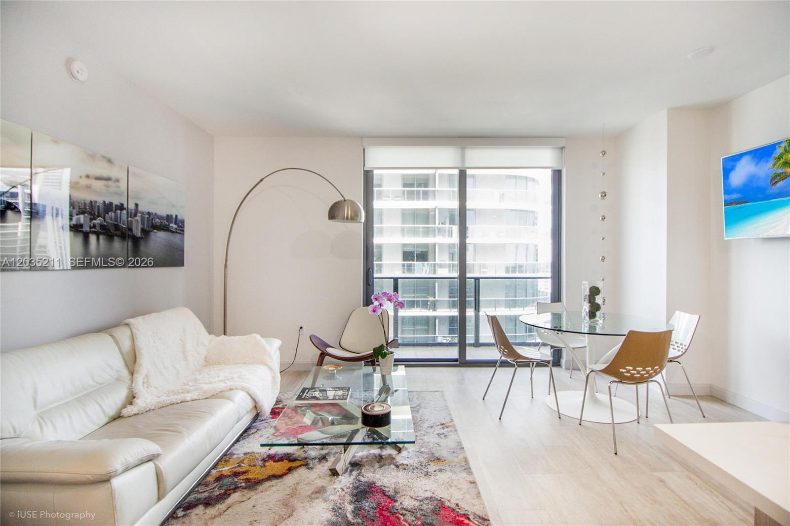 A modern living and dining area features a white sofa, glass coffee table, and balcony — 55 SW 9th St # 3802, Miami FL 33130, MIAMI, FL