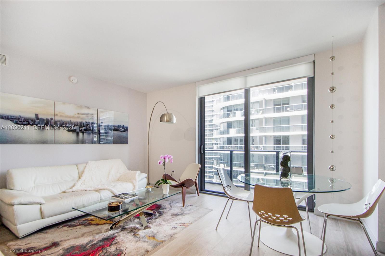A modern living and dining area features a white sofa, glass tables, and floor-to-ceiling windows — 55 SW 9th St # 3802, Miami FL 33130, MIAMI, FL