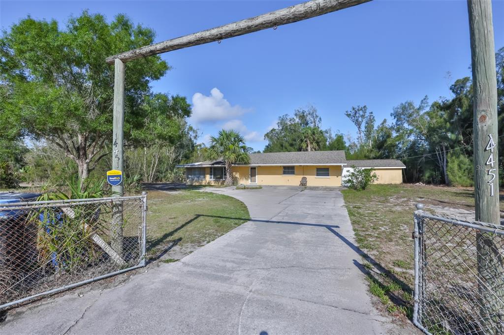 A yellow single-story house sits behind a chain-link fence and a wooden overhead gate — 14451 HIGHLAND ROAD, WIMAUMA, FL