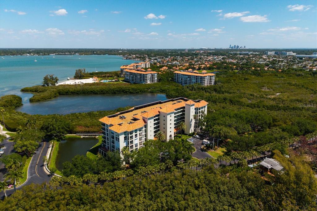 An aerial view shows a multi-story residential building surrounded by dense trees and water — 4801 OSPREY DRIVE S UNIT 207, ST PETERSBURG, FL