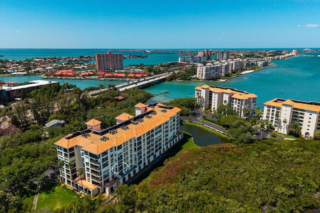 An aerial view shows a multi-story apartment building surrounded by lush trees and coastal waters — 4801 OSPREY DRIVE S UNIT 207, ST PETERSBURG, FL