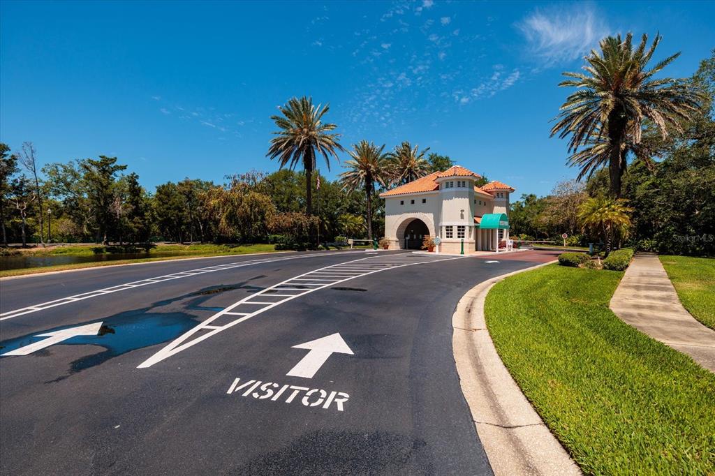 A gated community entrance features a guardhouse, palm trees, and a paved visitor lane — 4801 OSPREY DRIVE S UNIT 207, ST PETERSBURG, FL