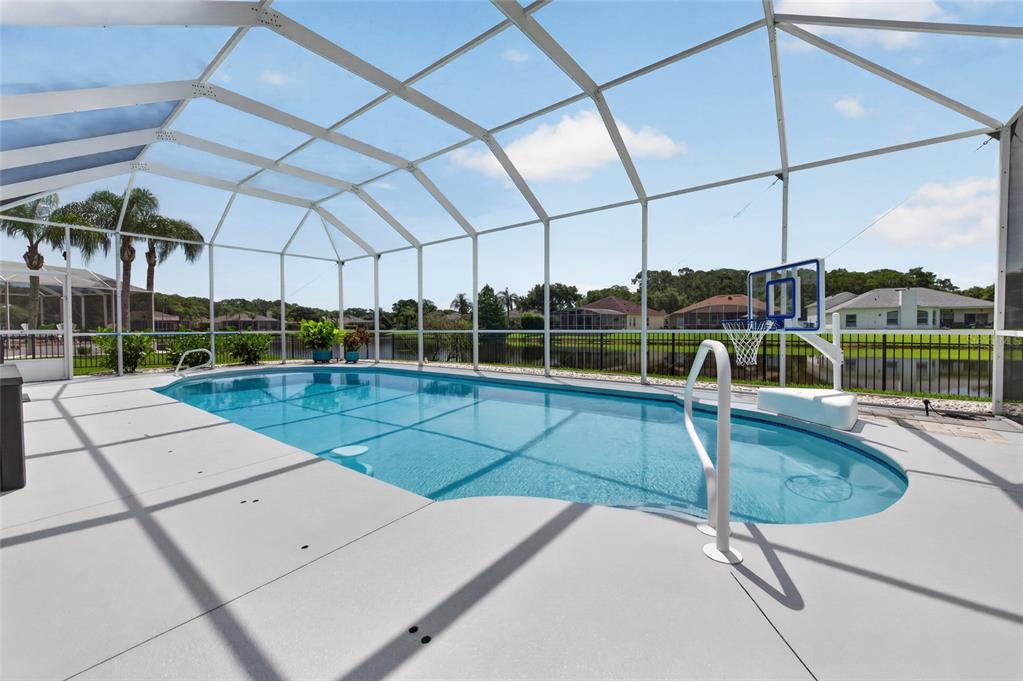 A screened-in swimming pool with a basketball hoop sits on a patio overlooking a lake — 1747 TRIBUTORY LANE, PORT ORANGE, FL