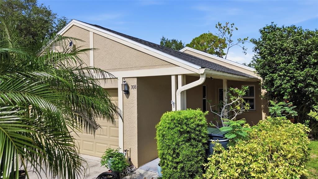 The exterior of a tan house features a garage, a covered entryway, and surrounding landscaping — 308 CHARTLEY COURT N, SARASOTA, FL