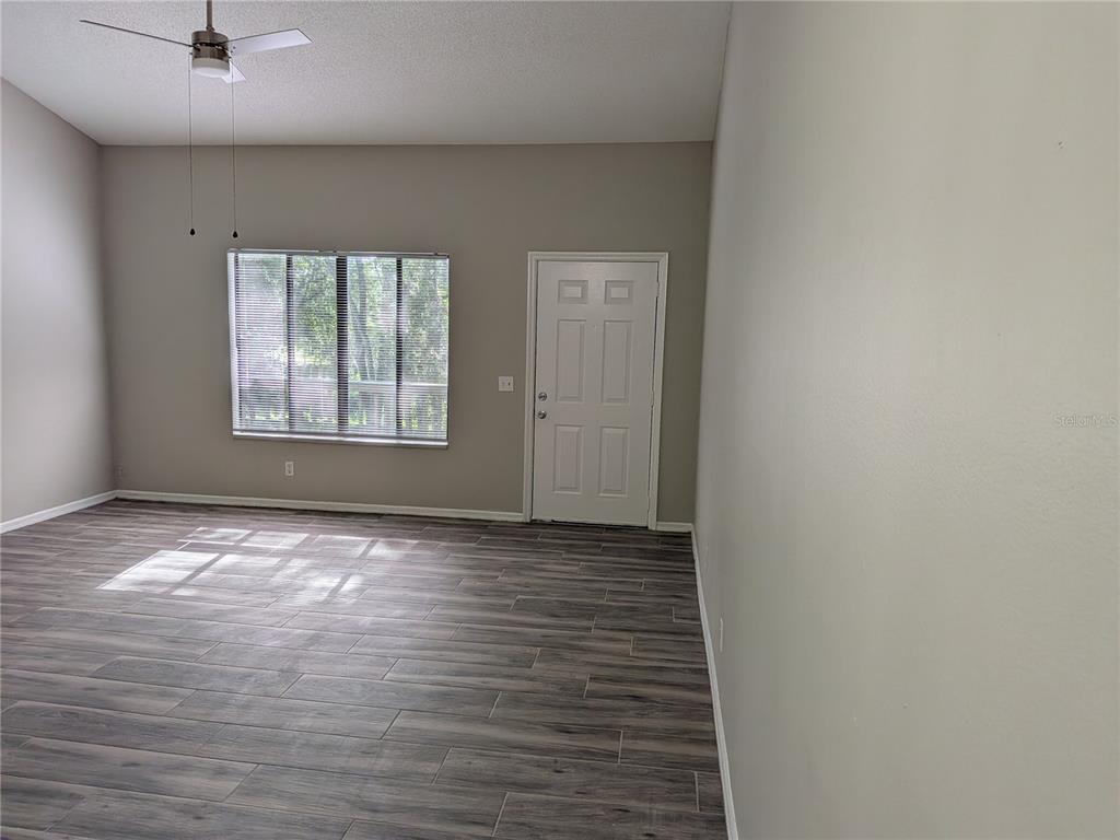 An empty room with gray wood-look flooring, a ceiling fan, a window, and a door — 1020 HOWELL UNIT A7, BROOKSVILLE, FL
